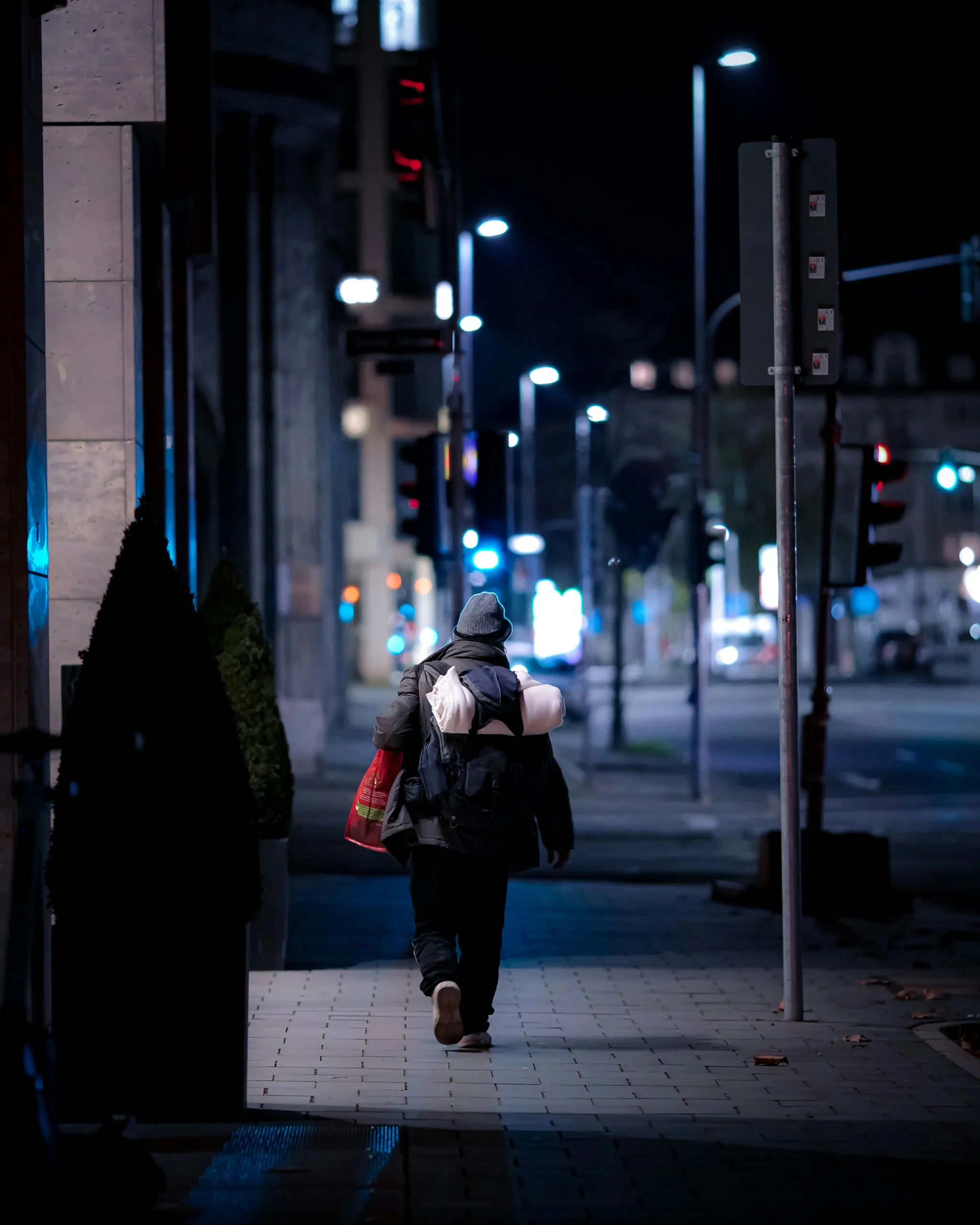 femme en veste noire et pantalon noir marchant sur le trottoir pendant la nuit