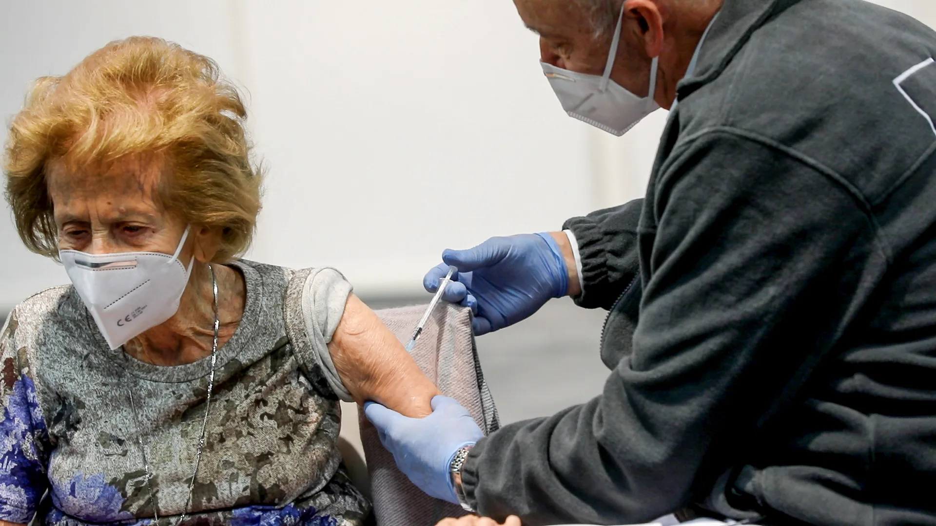 Une personne âgée en train d'être piquée à l'épaule par un médecin.