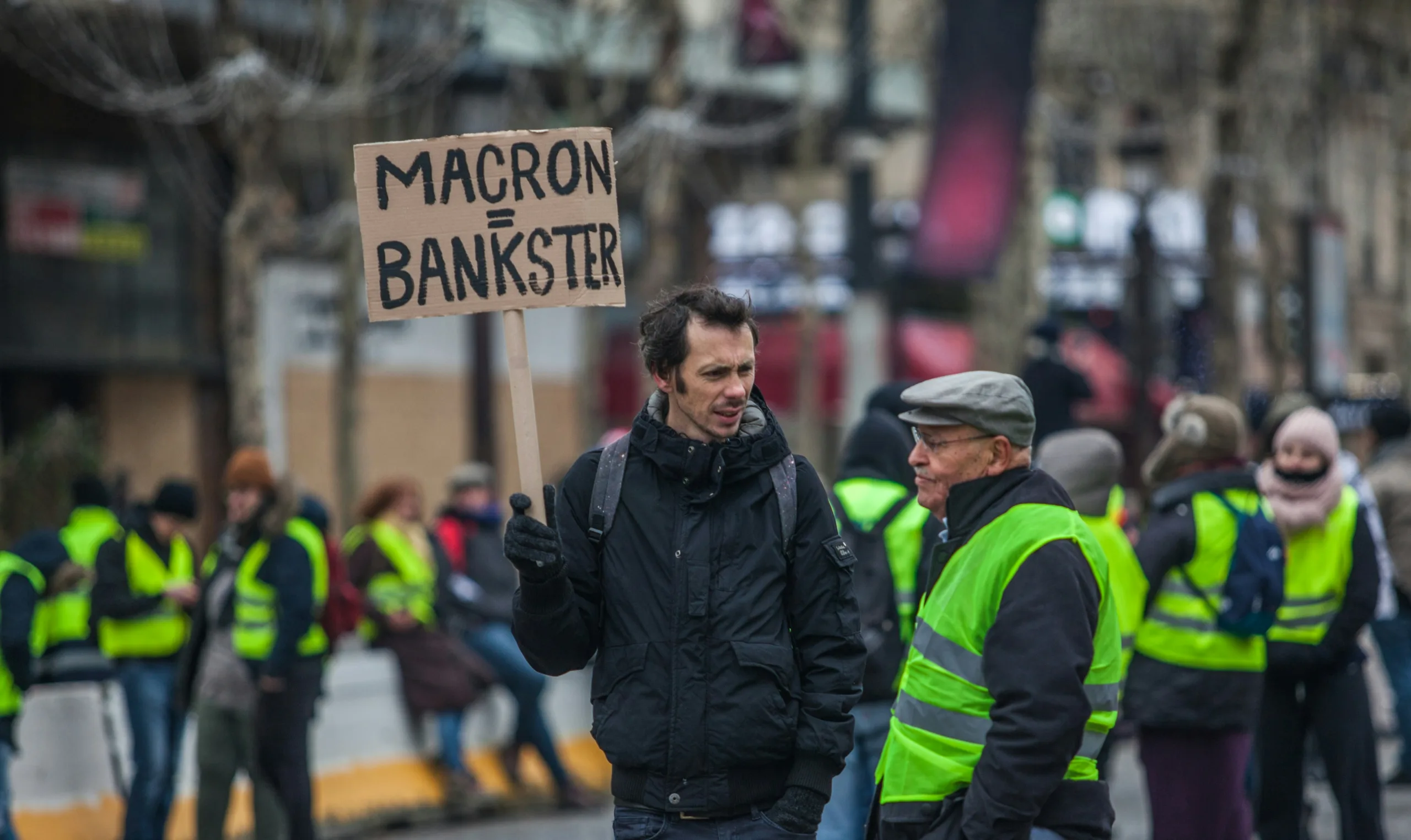 Manifestation gilets jaune, homme tenant une pancarte "Macron Bankster"